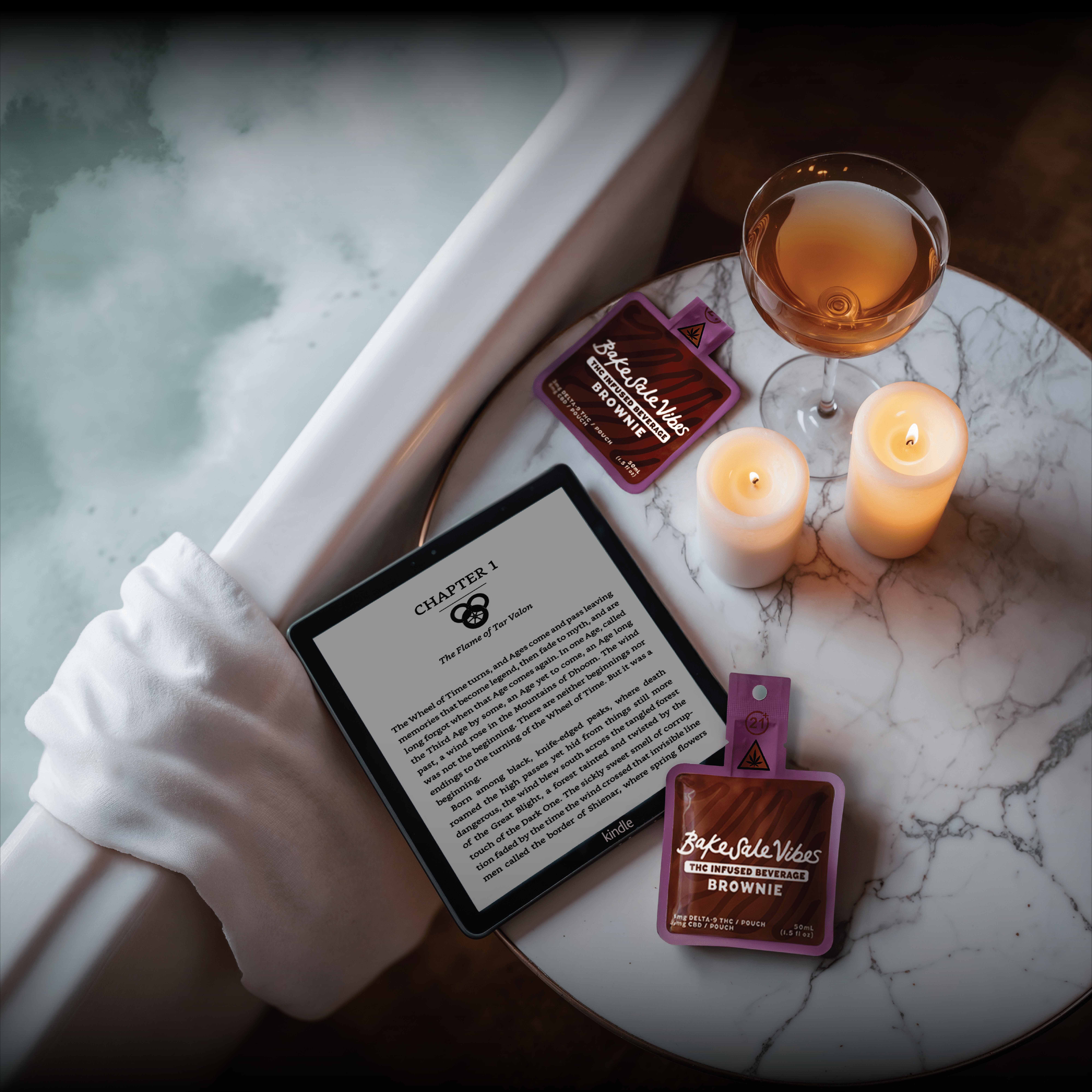 Relaxing bath scene with BakeSale Vibes products, candles, and tablet